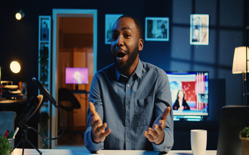 Happy influencer in home studio using professional camera and mic to film live broadcast for online streaming platforms, interacting with fans. BIPOC online star hosts q a session with viewers