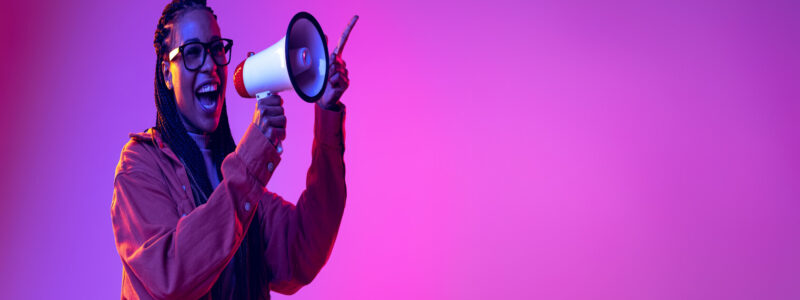 Portrait of yougn stylish girl shouting in megaphone isolated over gradient pink purple background