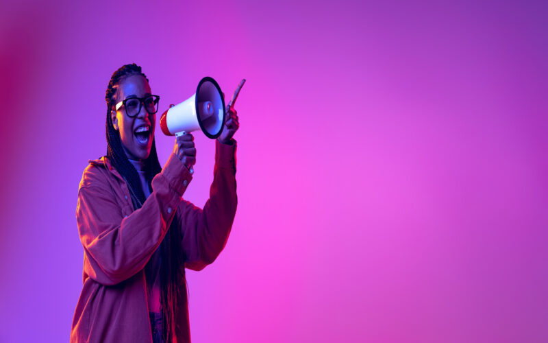 Portrait of yougn stylish girl shouting in megaphone isolated over gradient pink purple background